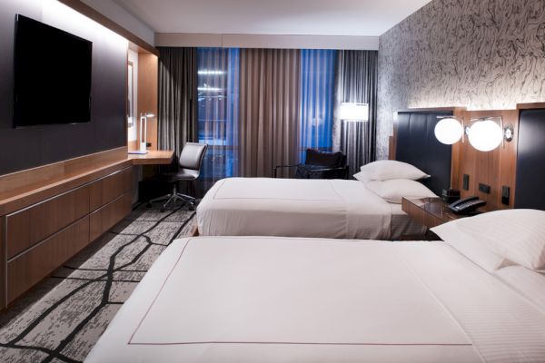 A modern hotel room with two neatly made beds, a flat-screen TV, a work desk, and contemporary decor on the walls.