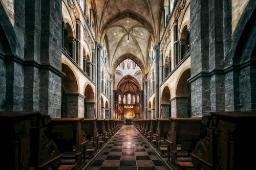 The image shows the interior of a grand, Gothic-style church with high vaulted ceilings, ornate arches, and rows of pews lining the checkered floor.