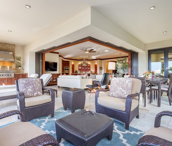 This image shows a spacious and modern indoor-outdoor living area with comfortable seating, a dining table, and a view into a well-furnished interior.