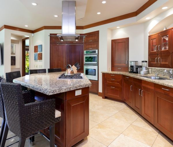 The image shows a modern kitchen with wooden cabinetry, granite countertops, and bar seating, creating a stylish, inviting space.
