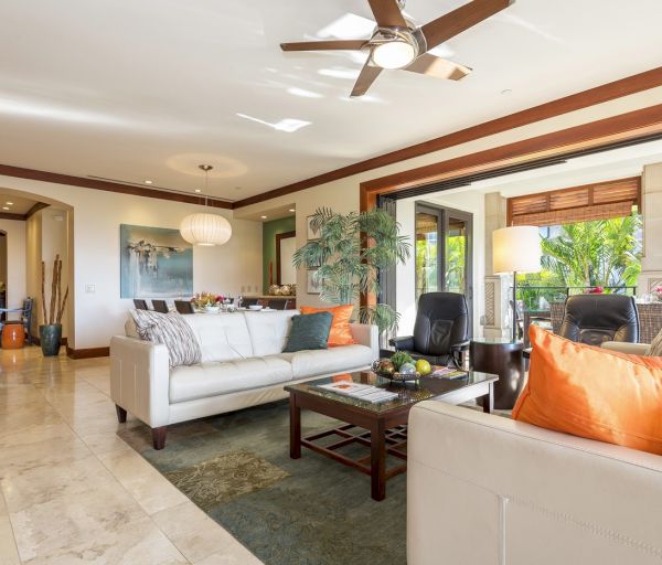 A stylish, bright living room featuring a white sofa, orange cushions, a wooden coffee table, and large windows with garden views.
