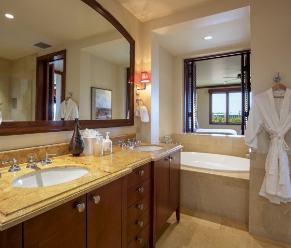 The image depicts a stylish bathroom with a double sink, a large mirror, a bath, and a white robe hanging nearby.