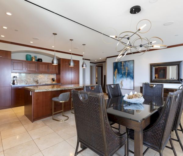 The image shows a modern kitchen and dining area with elegant lighting, dark wood cabinets, and a stylish dining table.