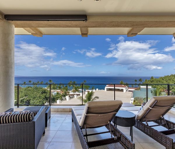 The image shows a luxurious balcony with lounge chairs, overlooking a stunning ocean view and a clear blue sky with clouds.