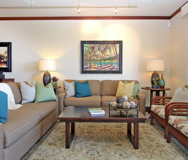 The image shows a cozy living room with a sofa, chairs, decorative pillows, a coffee table, and wall art in a bright setting.