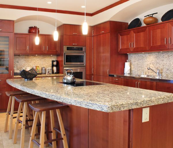 The image shows a modern kitchen with wooden cabinets, a granite countertop, and bar stools, creating a warm and inviting space.