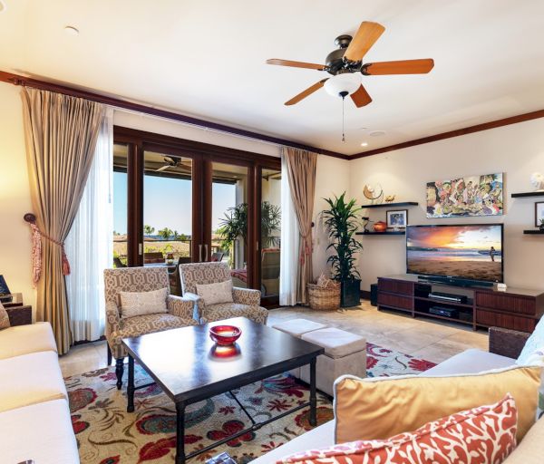 The image shows a cozy living room with a fan, comfortable seating, a coffee table, and sliding glass doors leading outside.