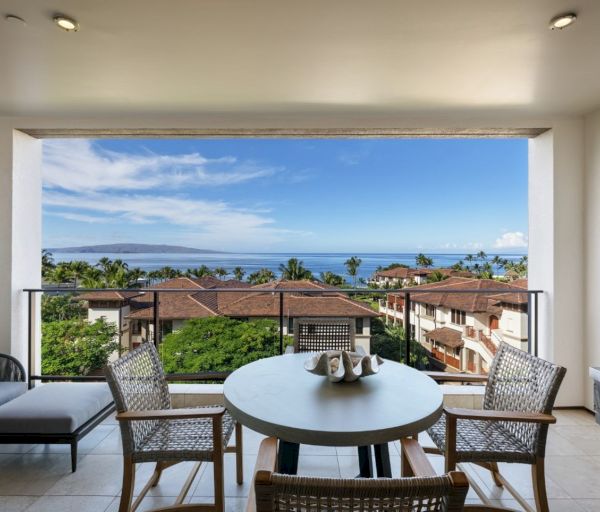 The image shows a stylish indoor seating area with a view of the ocean and surrounding landscape through a large window.