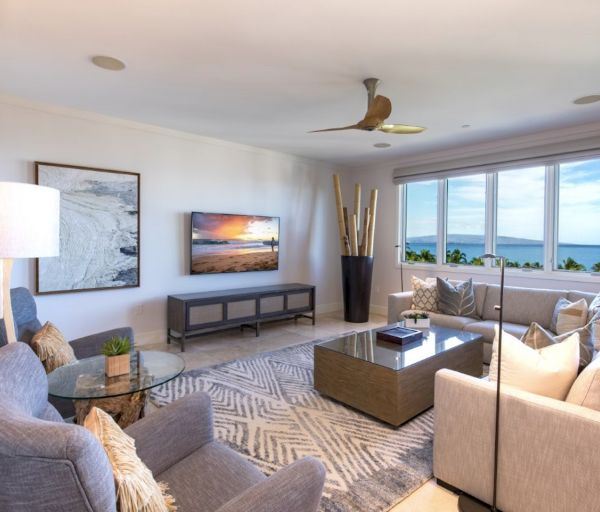 The image depicts a modern living room with light-colored furniture, a large window showing a view, and tasteful decor.