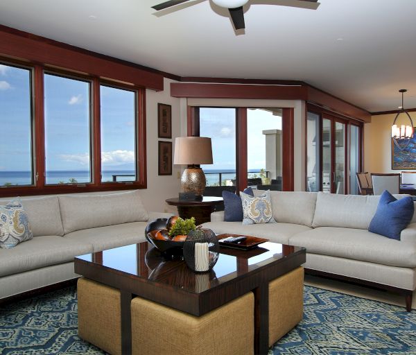A modern living room with ocean views, featuring a large gray sectional sofa, wooden coffee table, floor lamp, blue rug, and open dining area.