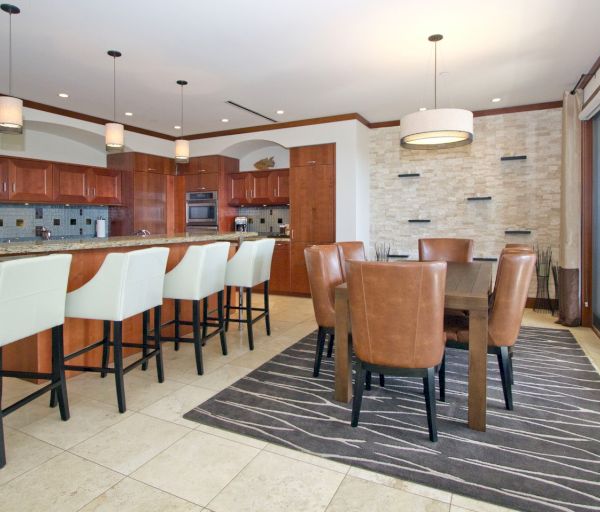 The image features a modern kitchen with a breakfast bar, dining area, wooden cabinets, and stylish light fixtures.