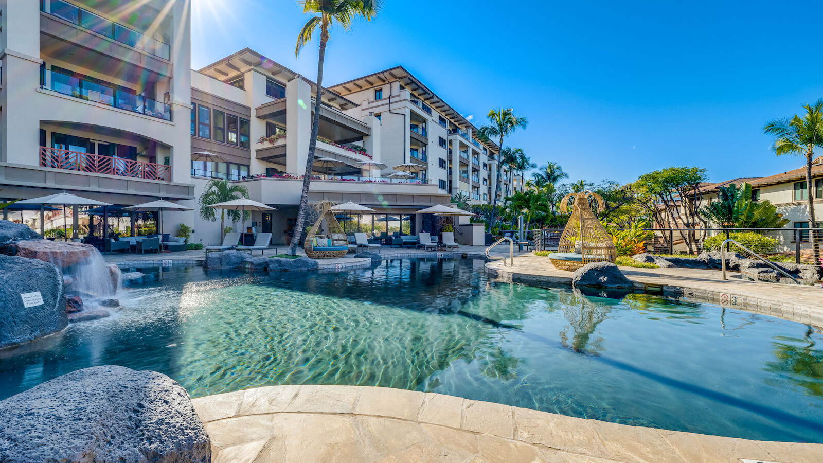The image shows a sunny pool area at a resort, featuring lounge chairs, palm trees, and modern architecture. A perfect getaway.