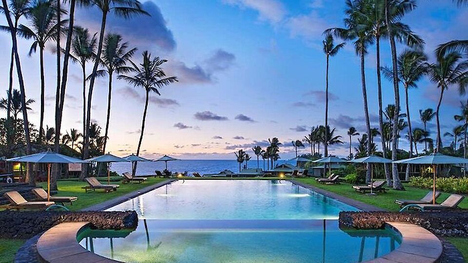 A tropical resort pool scene with palm trees, lounge chairs, and a calm ocean beyond at sunset, inviting and serene.