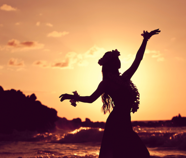 Silhouette of a person dancing on the beach at sunset, arms raised, waves behind, warm orange-pink sky.