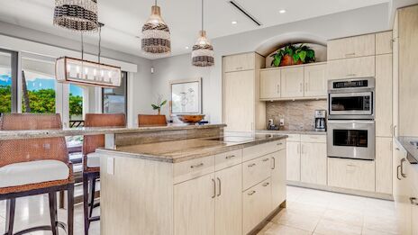 A bright, modern kitchen with light wood cabinets, an island, tile floor, stainless appliances, pendant lights, and a dining area nearby, all airy.