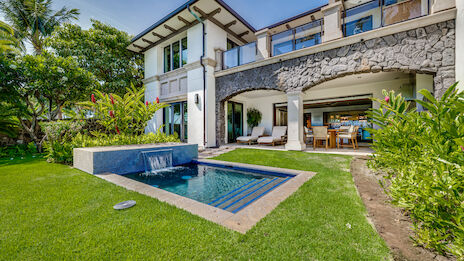 A modern two-story house with a stone accent, outdoor pool and spa, lush lawn, and a covered patio perfect for lounging and dining.