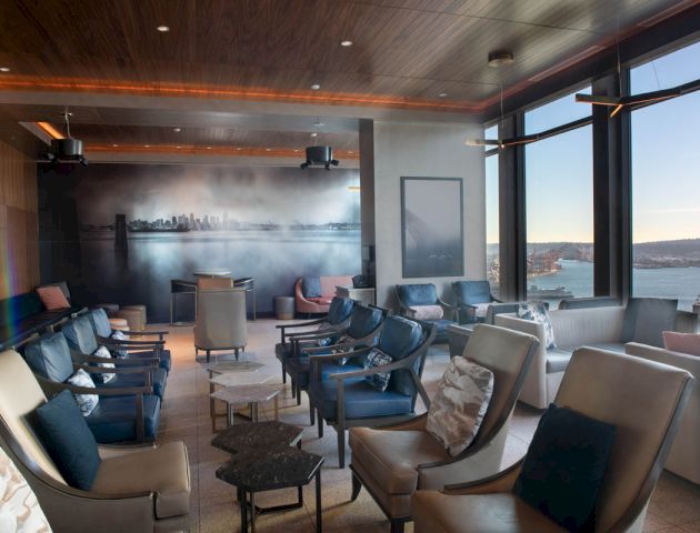 A modern lounge area with rows of seating overlooks a scenic waterfront, featuring a mural of a skyline and large floor-to-ceiling windows.