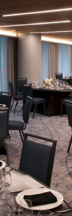 The image shows an elegantly set banquet hall, with round tables, black tablecloths, formal dinner settings, and floral centerpieces.